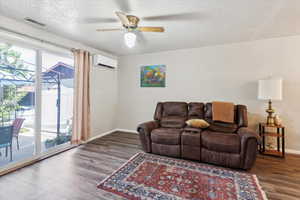 Living area with a wall mounted AC, wood finished floors, baseboards, a textured ceiling, and ceiling fan