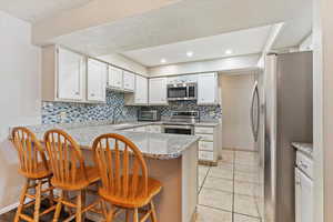 Kitchen featuring appliances with stainless steel finishes, decorative backsplash, white cabinetry, a peninsula, and a breakfast bar area