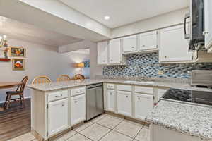 Kitchen featuring backsplash, white cabinets, a peninsula, light tile patterned floors, and appliances with stainless steel finishes