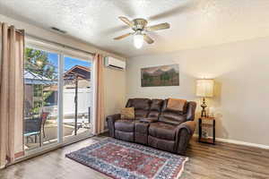 Living room featuring a textured ceiling, light wood-type flooring, a ceiling fan, and a wall mounted air conditioner