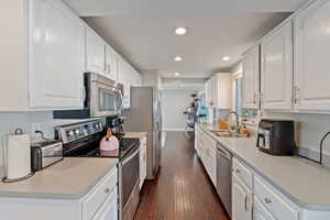 Kitchen with appliances with stainless steel finishes, a sink, dark wood finished floors, recessed lighting, and white cabinetry
