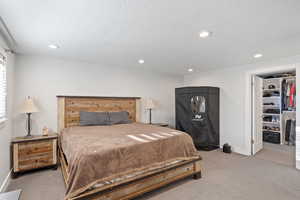 Primary Bedroom with light carpet, recessed lighting, baseboards, and a walk in closet