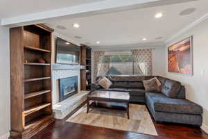Living area featuring crown molding, wood-type flooring, a fireplace, recessed lighting, and baseboards