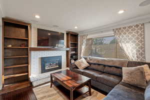 Living room with crown molding, wood-type flooring, a brick fireplace, recessed lighting, and built in features