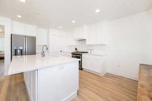 Kitchen featuring a sink, appliances with stainless steel finishes, light wood-style floors, white cabinetry, and recessed lighting