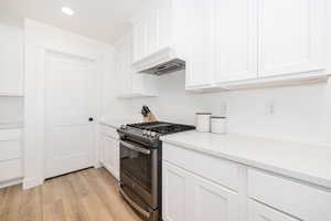 Kitchen with gas stove, light wood-type flooring, premium range hood, white cabinets, and recessed lighting
