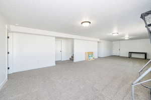 Finished below grade area with carpet flooring, stairway, baseboards, and a textured ceiling