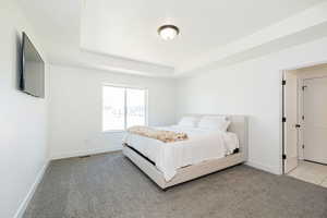 Bedroom with baseboards, a tray ceiling, and light carpet