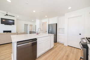 Kitchen featuring stainless steel appliances, a sink, open floor plan, light wood-style floors, and white cabinets