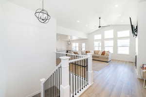 Hall with an upstairs landing, baseboards, wood finished floors, lofted ceiling, and recessed lighting