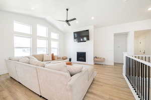 Living area featuring ceiling fan, light wood finished floors, a glass covered fireplace, baseboards, and high vaulted ceiling