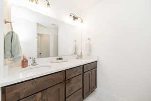Full bath featuring double vanity, marble finish floors, and baseboards