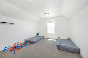 Unfurnished bedroom with a wall mounted air conditioner, lofted ceiling, carpet flooring, and baseboards