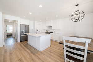 Kitchen with stainless steel appliances, a sink, a chandelier, light wood-style floors, and white cabinetry