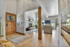 Entryway featuring a stone fireplace, light wood finished floors, baseboards, a textured ceiling, and high vaulted ceiling
