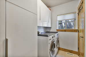 Washroom with cabinet space, independent washer and dryer, light tile patterned flooring, and baseboards
