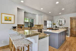 Kitchen featuring a center island, a textured ceiling, white cabinets, a sink, and backsplash