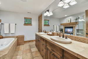 Full bathroom featuring double vanity, a tub with jets, stone tile flooring, a skylight, and a fireplace