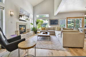 Living room featuring high vaulted ceiling, light wood finished floors, and a stone fireplace