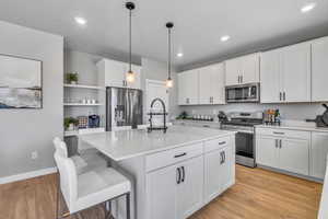 Kitchen featuring stainless steel appliances, open shelves, white cabinetry, decorative light fixtures, and an island