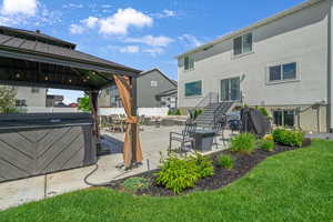 Back of house with an outdoor living space  a gazebo, hot tub  and a patio.