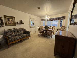 Dining area featuring ornamental molding, a chandelier, light colored carpet, a textured ceiling, and baseboards