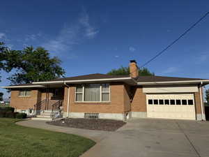 Ranch-style house featuring a garage, concrete driveway, brick siding, a chimney, and a front lawn