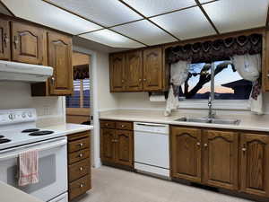 Kitchen featuring white appliances, a sink, under cabinet range hood, and light countertops