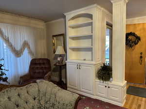 Living area with wood finished floors, built in features, baseboards, ornamental molding, and ornate columns
