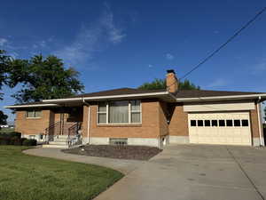 Ranch-style house with a garage, brick siding, a chimney, driveway, and a front lawn