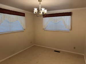 Unfurnished room featuring a chandelier, carpet, baseboards, and crown molding