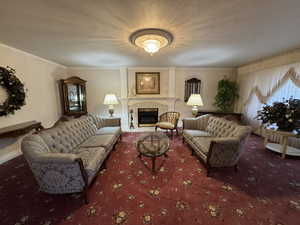 Living area with carpet flooring, a textured ceiling, a fireplace, and ornamental molding