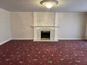 Unfurnished living room with carpet, a tiled fireplace, ornamental molding, baseboards, and a textured ceiling