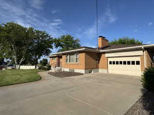 Single story home featuring concrete driveway, brick siding, an attached garage, and a chimney