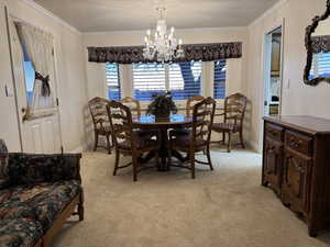 Dining space with a chandelier, light carpet, crown molding, baseboards, and a textured ceiling
