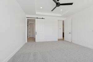 Unfurnished bedroom with a barn door, a tray ceiling, carpet floors, recessed lighting, and a ceiling fan