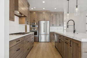 Kitchen with stainless steel appliances, a kitchen island with sink, backsplash, light wood-style floors, and decorative light fixtures