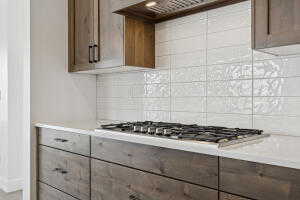 Kitchen featuring stainless steel gas cooktop, backsplash, ventilation hood, and light countertops