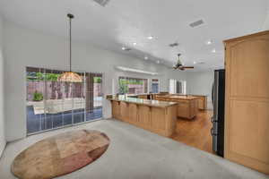 Kitchen featuring freestanding refrigerator, recessed lighting, ceiling fan, a kitchen breakfast bar, and light stone counters