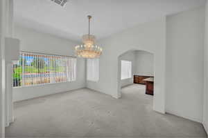 Unfurnished room with light colored carpet, a chandelier, arched walkways, and baseboards