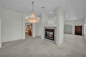 Unfurnished living room featuring arched walkways, a chandelier, a tile fireplace, carpet flooring, and recessed lighting