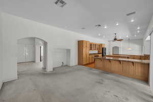 Kitchen with arched walkways, fridge with ice dispenser, a ceiling fan, a kitchen breakfast bar, and brown cabinets