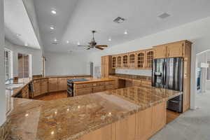 Kitchen with black fridge with ice dispenser, a sink, arched walkways, a ceiling fan, and a center island with sink