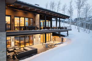 Snow covered house featuring an outdoor living space with a fire pit, stone siding, and a patio area