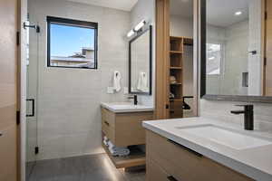 Bathroom with a shower stall, two vanities, tile walls, and tile patterned flooring