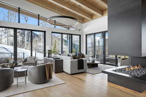 Living area with wooden ceiling with exposed beams, wood finished floors, plenty of natural light, a towering ceiling, and french doors