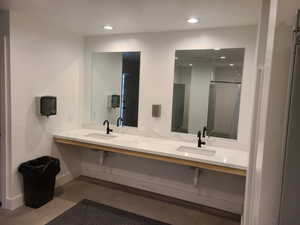 Bathroom with baseboards, recessed lighting, finished concrete floors, double vanity, and a shower with shower door