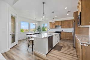 Kitchen featuring brown cabinets, light stone countertops, a chandelier, light wood finished floors, and hanging light fixtures