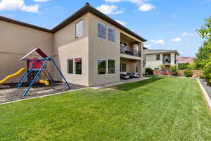 Rear view of house with a playground, stucco siding, a balcony, and a patio