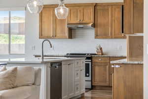 Kitchen with brown cabinetry, tasteful backsplash, appliances with stainless steel finishes, and light stone counters